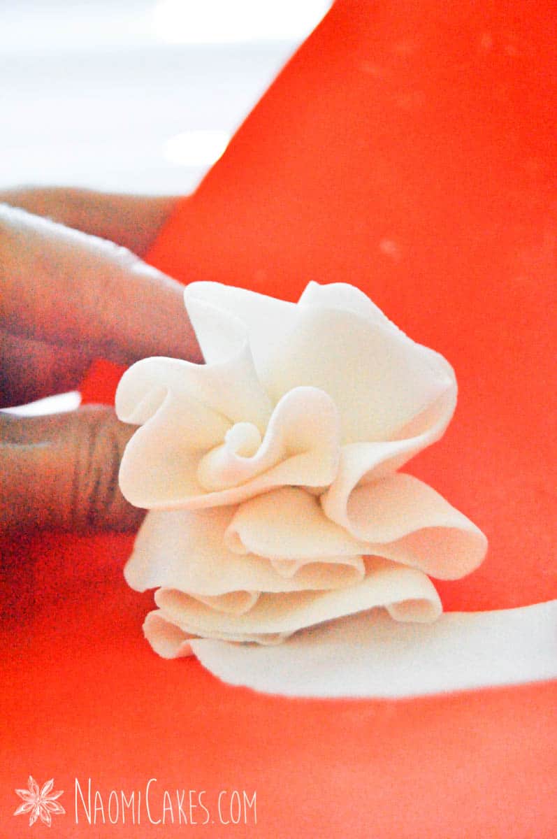 hand holding a bundle of fondant ruffles by an orange background