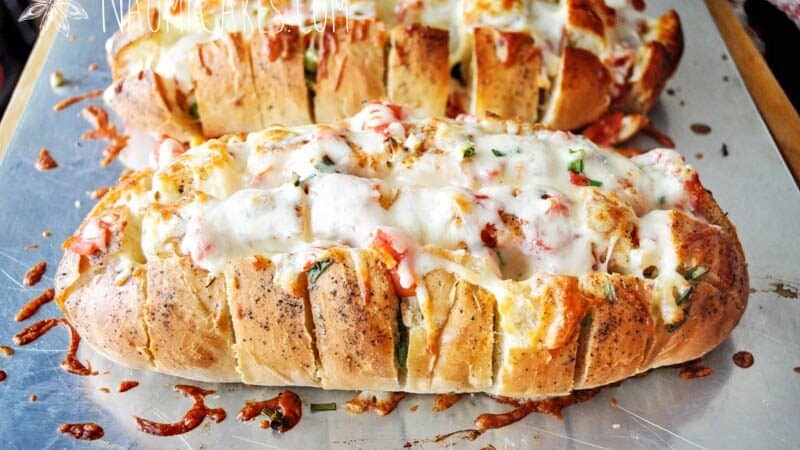 2 loaves of fresh cheesy garlic bread on a pan