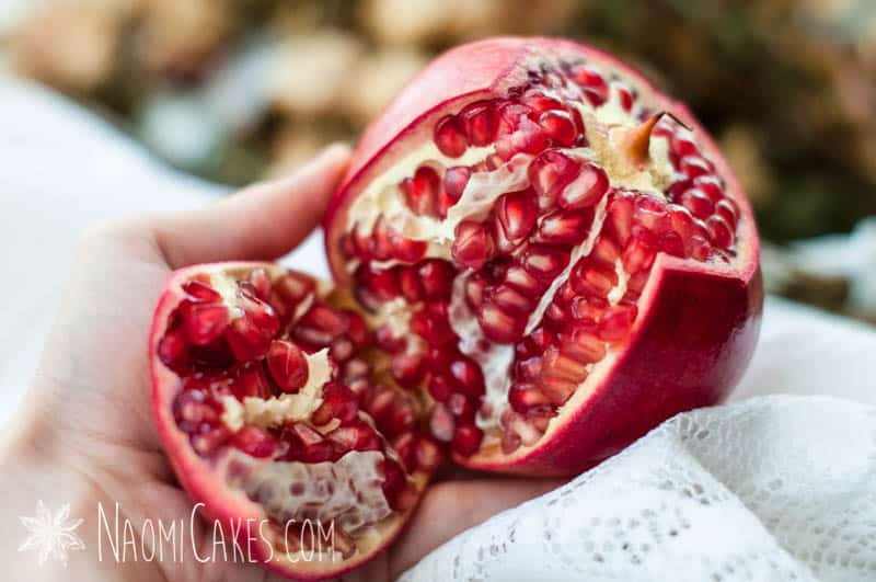 hand holding a cut open pomegranate with the seeds exposed