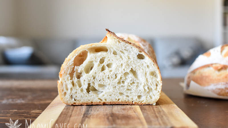 half a loaf of cut white sourdough bread to show the crumb on a wooden cutting board