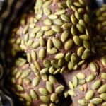 close up of a square baked dark rye pumpkinseed covered roll in a bowl with a checked cloth