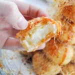 hand holding a cream puff from a croquembouche with a bite taken out and the cream showing on the inside